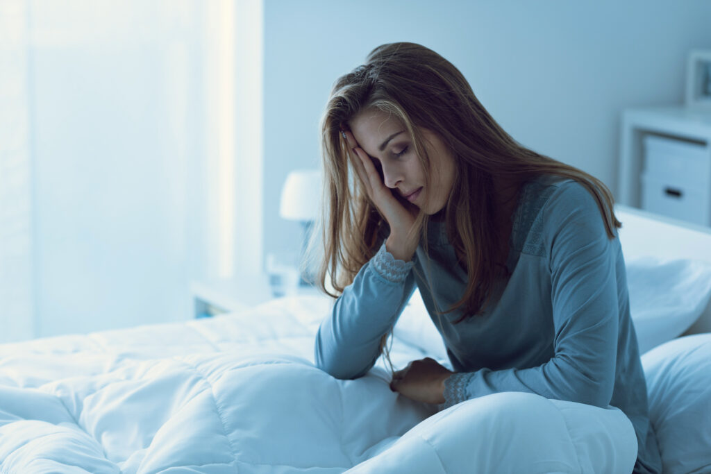 Woman holding head in bed fatigued from stress