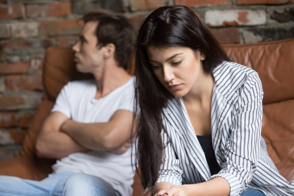 young couple arguing, woman enabling actions of partner looking down and sad.