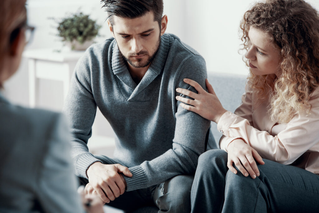 Young couple in therapy sessions discussing infidelity. Woman's hand is placed on the man's arm offering support.