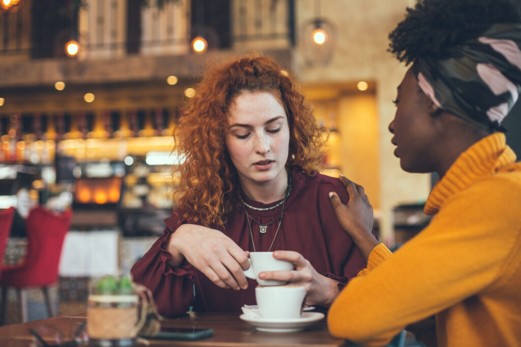 two young woman sitting in cafe, one woman offering support to other going through change