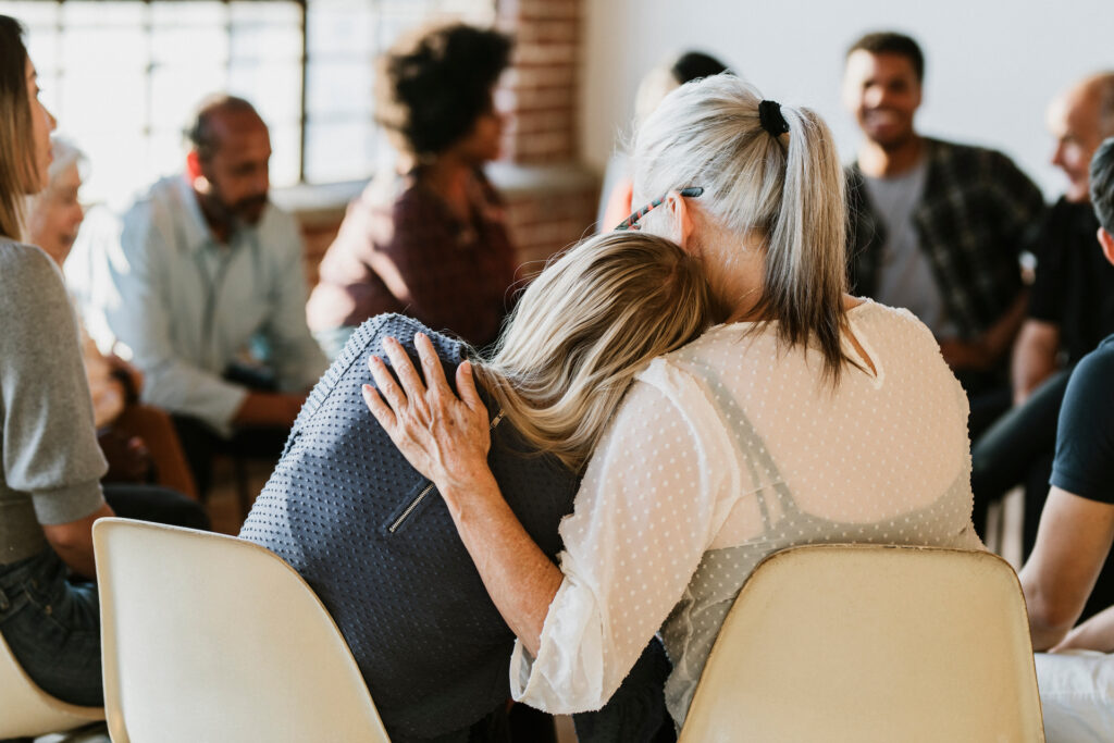 woman holding another woman in a side embrace offering support during group therapy