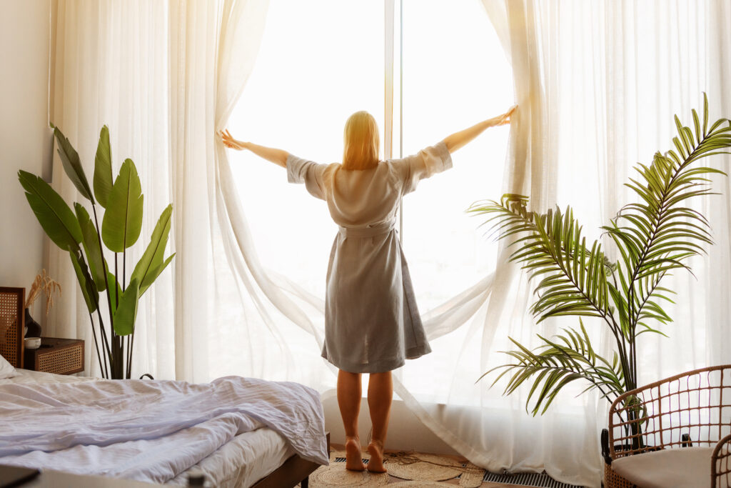 woman opening curtains to sun feeling good about mental health